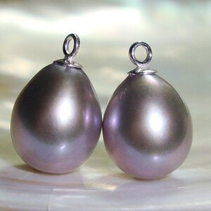 May include: Two pearlescent gray teardrop-shaped pendants with silver jump rings. The pendants are smooth and have a subtle iridescent sheen.