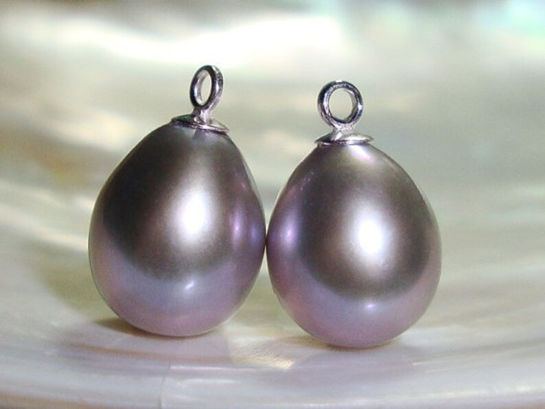 May include: Two pearlescent gray teardrop-shaped pendants with silver jump rings. The pendants are smooth and have a subtle iridescent sheen.