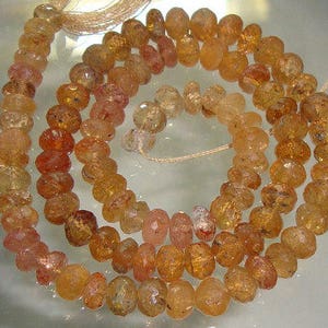 May include: A strand of orange and brown gemstone beads. The beads are faceted and have a slightly irregular shape. The beads are strung on a thin cord.