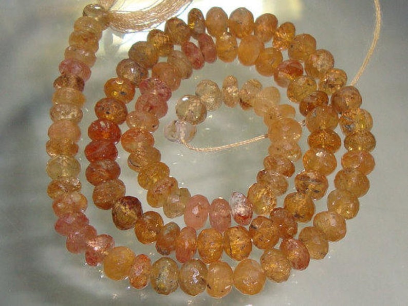 May include: A strand of orange and brown gemstone beads. The beads are faceted and have a slightly irregular shape. The beads are strung on a thin cord.