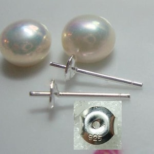 Puede incluir: Un par de pendientes de perlas blancas con postes y respaldos de plata. Los respaldos están marcados con "925", lo que indica que están hechos de plata de ley.