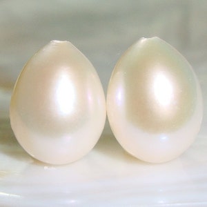 May include: Two white pearlescent oval-shaped pearls on a white background.