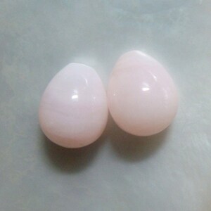 Puede incluir: Dos piedras de color rosa en forma de l&aacute;grima. Las piedras son lisas y pulidas.
