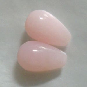 May include: Two teardrop-shaped pink opal beads. The beads are smooth and have a glossy finish.