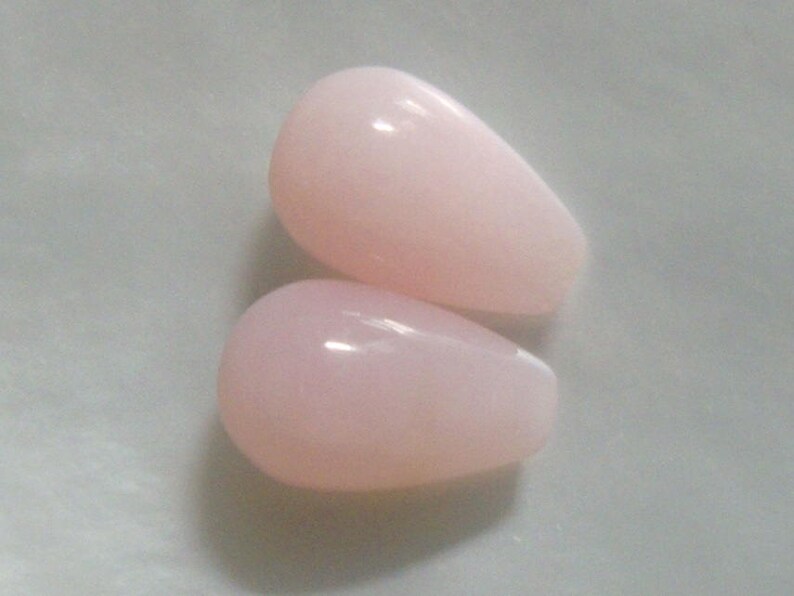 May include: Two teardrop-shaped pink opal beads. The beads are smooth and have a glossy finish.
