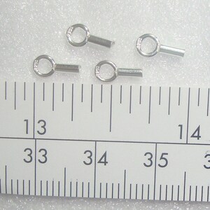 May include: Four silver jump rings with a small loop on one end and a straight pin on the other end. The jump rings are approximately 1.25 cm long and are measured on a ruler.