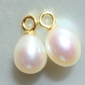 May include: Two pear-shaped, white pearl pendants with a gold-colored loop at the top. The pearls have a subtle pink iridescence. The pendants are likely for earrings or a necklace, showcasing a classic jewelry design.