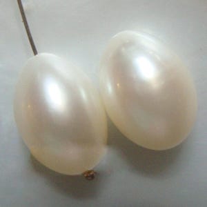 May include: Two white oval-shaped pearls with a smooth, glossy finish.