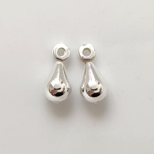 May include: Two silver teardrop-shaped charms with a loop at the top.