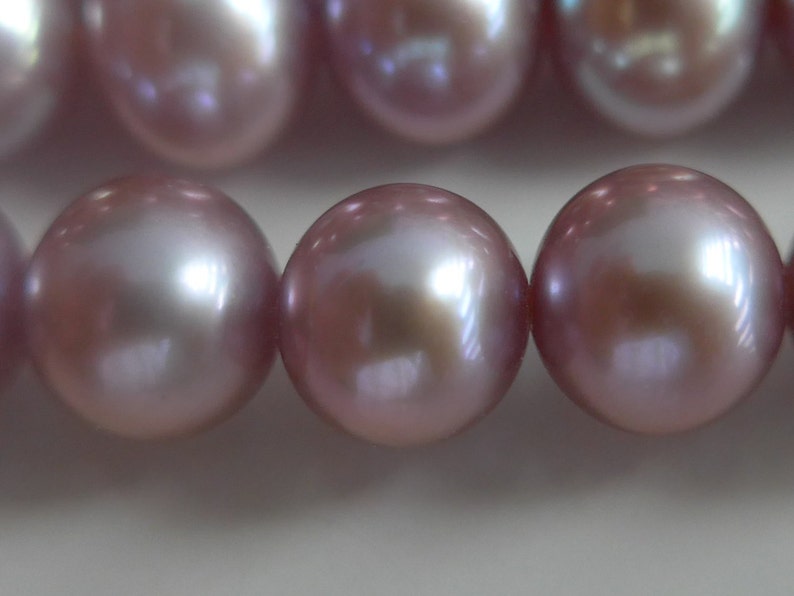 May include: A strand of iridescent pink pearls. The pearls are round and smooth, with a subtle shimmer.