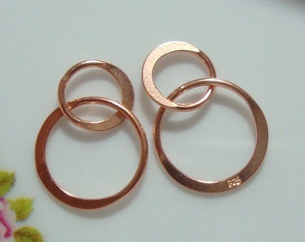 May include: Two pairs of interlocking rose gold-toned circular rings. Each pair consists of a larger ring connected to a smaller ring. The metal surface is smooth and reflective. One of the larger rings features a small 925 stamp.