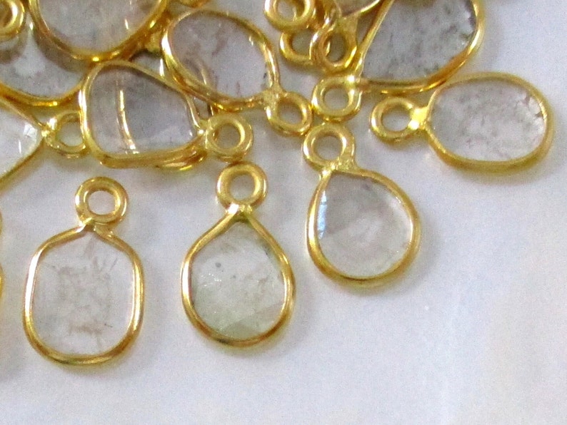 May include: A group of gold-plated teardrop-shaped pendants with clear glass or crystal stones. The pendants have a loop at the top for attaching to a chain or cord.