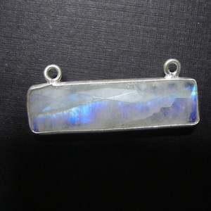 May include: A silver pendant with a rectangular moonstone gemstone. The stone has a white base with blue and purple iridescent flashes.
