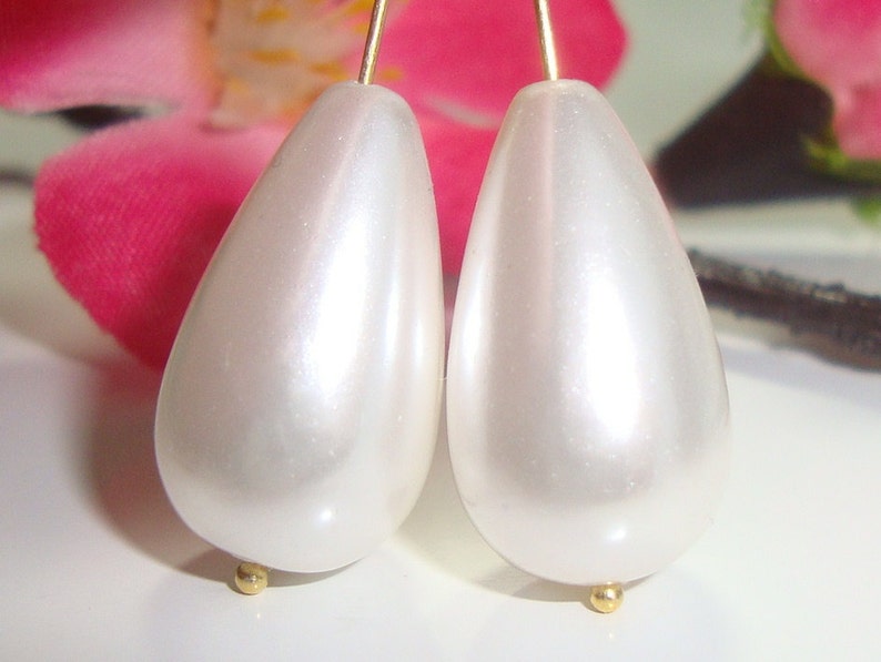 Puede incluir: Un par de pendientes blancos en forma de pera con detalles dorados.