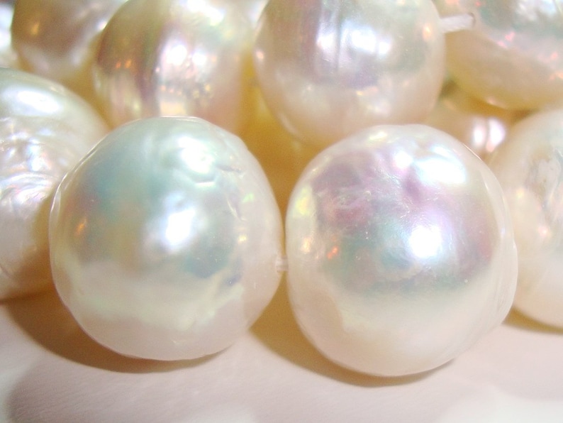 May include: A strand of white pearls with an iridescent sheen. The pearls are round and smooth, and they are arranged in a line.