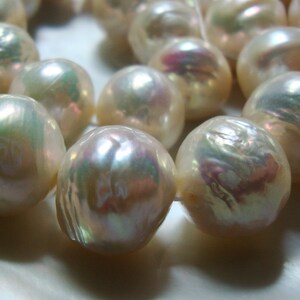 May include: A strand of iridescent white pearls with a slight pink hue. The pearls are strung on a white thread and are of varying sizes.