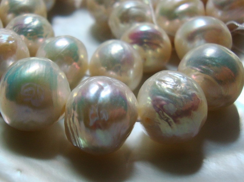 May include: A strand of iridescent white pearls with a slight pink hue. The pearls are strung on a white thread and are of varying sizes.