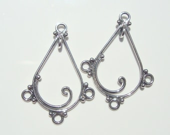 May include: Two silver earring findings with a teardrop shape and a decorative swirl design. Each finding has three loops for attaching jewelry components.