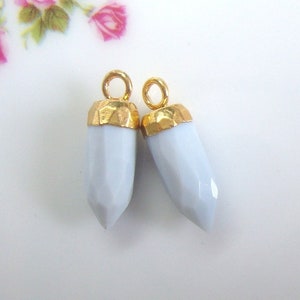May include: Two light blue gemstone pendants with gold-toned metal caps and loops. The gemstones are faceted and have a pointed shape.