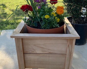 Könnte beinhalten: Ein Holz-Pflanzgefäß mit einem braunen Blumentopf im Inneren. Das Pflanzgefäß ist aus hellem Holz gefertigt und hat eine natürliche Oberfläche. Der Blumentopf ist mit einer Vielzahl von bunten Blumen gefüllt, darunter rote, lila, gelbe und orangefarbene.