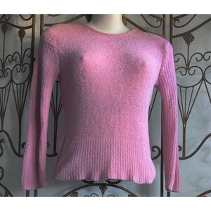 May include: A light pink sweater with a crew neck and long sleeves. The sweater has a ribbed hem and cuffs. The fabric appears to be soft and fuzzy. The sweater is displayed on a mannequin.