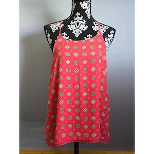 May include: A sleeveless tank top in a vibrant coral pink hue, featuring a repeating geometric pattern of small, stylized star-like shapes in white, black, and yellow. The garment has thin spaghetti straps and a rounded neckline.