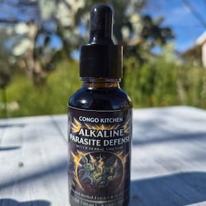 Puede incluir: Una botella de vidrio ámbar oscuro con un cuentagotas negro. La etiqueta dice "CONGO KITCHEN ALKALINE PARASITE DEFENSE BITTER HERBAL TINCTURE." La botella contiene 30 ml de extracto de hierbas líquido. El fondo está borroso con follaje verde y cielo azul.