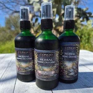 May include: Three green glass spray bottles of "Herbal Home Defence" from Congo Kitchen. The bottles have black caps and labels with botanical illustrations. The text "Kills Mold and Mildew" is visible on one label.