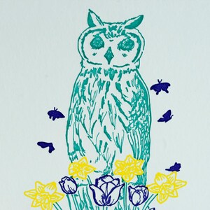 May include: A teal blue owl with yellow daffodils and purple tulips at its feet.  There are several small purple butterflies flying around the owl.