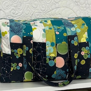 Peut inclure: Un sac fourre-tout rectangulaire en tissu avec un motif patchwork composé de bandes verticales dans des tons bleu sarcelle, vert citron, bleu marine et blanc. Le design présente des motifs circulaires, des lignes géométriques et deux anses.
