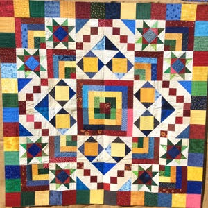 Könnte beinhalten: Ein farbenfroher Quilt mit verschiedenen geometrischen Mustern in Rot-, Blau-, Grün-, Gelb- und Weißtönen. Der Quilt besteht aus Quadraten und Dreiecken, und die Muster sind in einem symmetrischen Design angeordnet.