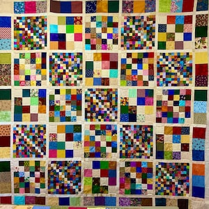 May include: A patchwork quilt featuring a grid of large squares, each composed of smaller multi-colored fabric squares in various patterns and solid colors. The entire grid is separated by thin, light cream-colored fabric sashing strips.