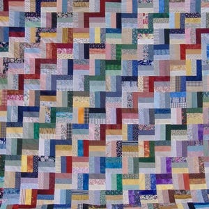 May include: A handmade quilt with a patchwork design. The quilt features a variety of fabrics in a range of colors, including blue, green, red, and yellow. The pattern is a series of zigzags, creating a visually interesting texture. The quilt is likely for a bed or a decorative throw.