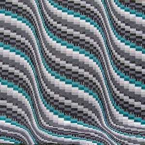 May include: A quilt with a geometric pattern of black, white, and teal squares. The squares are arranged in a diagonal pattern, creating a wave-like effect.