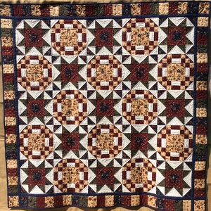 May include: A quilt with a geometric pattern in shades of brown, white, red, and blue. The quilt is made up of squares and triangles, and it has a border of blue and white stripes.