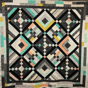 May include: A black and white quilt with geometric patterns in shades of teal, peach, and yellow. The quilt is made up of squares and diamonds, and the patterns are arranged in a symmetrical design.