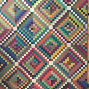 May include: A colorful quilt with a geometric pattern of squares in various shades of blue, green, red, orange, and yellow. The squares are arranged in a diagonal pattern, creating a sense of movement and depth.