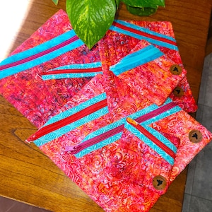 May include: Five colorful zippered pouches with a red, orange, and blue floral pattern. The pouches have a turquoise and red zipper tape. The pouches are made by "The Quilted Cat".