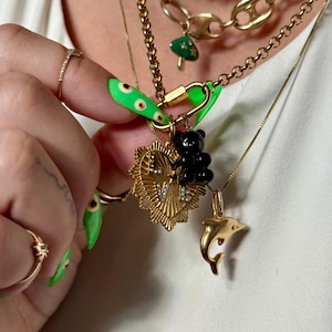 May include: Several gold necklaces are displayed, adorned with charms such as a black bear, a dolphin, and a heart pendant. The necklaces are layered, creating a fashionable appearance. The charms add a unique touch to the jewellery.