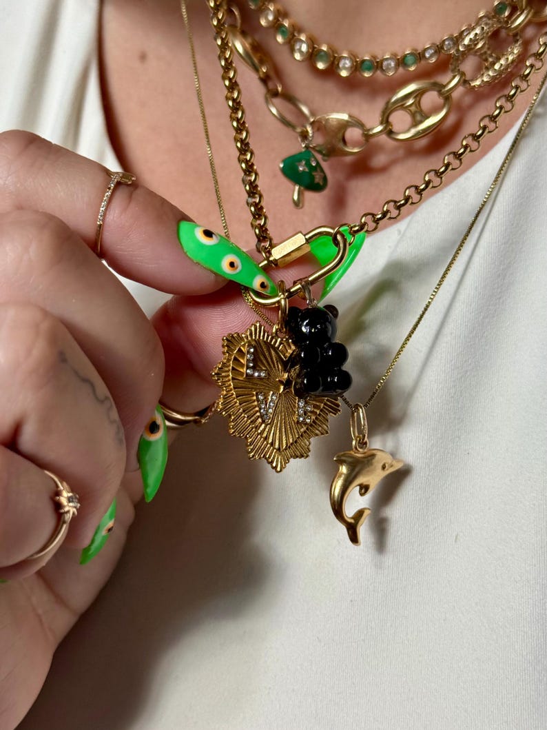 May include: Several gold necklaces are displayed, adorned with charms such as a black bear, a dolphin, and a heart pendant. The necklaces are layered, creating a fashionable appearance. The charms add a unique touch to the jewellery.