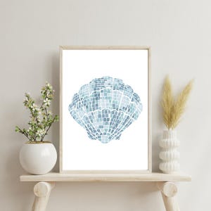 May include: A framed print featuring a blue seashell design. The artwork is composed of small, square tiles in varying shades of blue, creating a mosaic effect. The frame is a light wood color, and the print is displayed on a white wall.