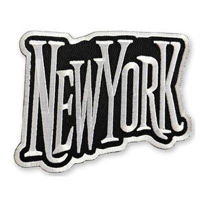 May include: An embroidered patch featuring the text NEW YORK in bold white capital letters with a black background and a white border. The lettering has a distinct serif font style with a slightly irregular, organic shape to the outer edge.