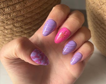 May include: A hand with painted fingernails. The nails are oval-shaped and painted in various shades of purple and pink. Some nails have a marbled design, while others feature glitter or striped accents. The overall aesthetic is feminine and stylish.
