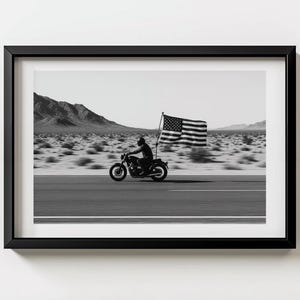 May include: Black and white framed print of a motorcycle rider carrying an American flag on a desert road. The image captures a sense of freedom and patriotism, with the flag waving in the wind.