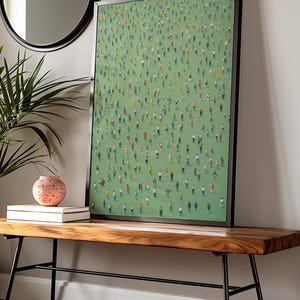 May include: A framed print of a painting depicting a large crowd of people standing on a green field. The print is hanging on a white wall above a wooden bench with black metal legs.