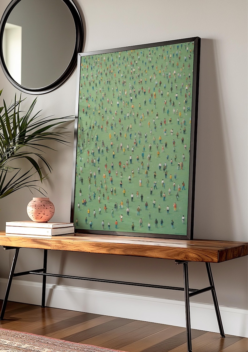 May include: A framed print of a painting depicting a large crowd of people standing on a green field. The print is hanging on a white wall above a wooden bench with black metal legs.