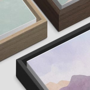 May include: Close-up of framed canvas art pieces. The artwork features watercolor landscape paintings in pastel colors. The frames are in various colors, including natural wood, dark brown, and black.
