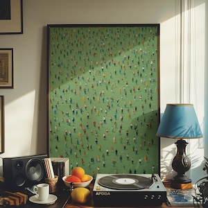 May include: A framed painting of a green field with hundreds of tiny people in various colors and poses. The painting is hanging on a wall above a record player and a lamp.