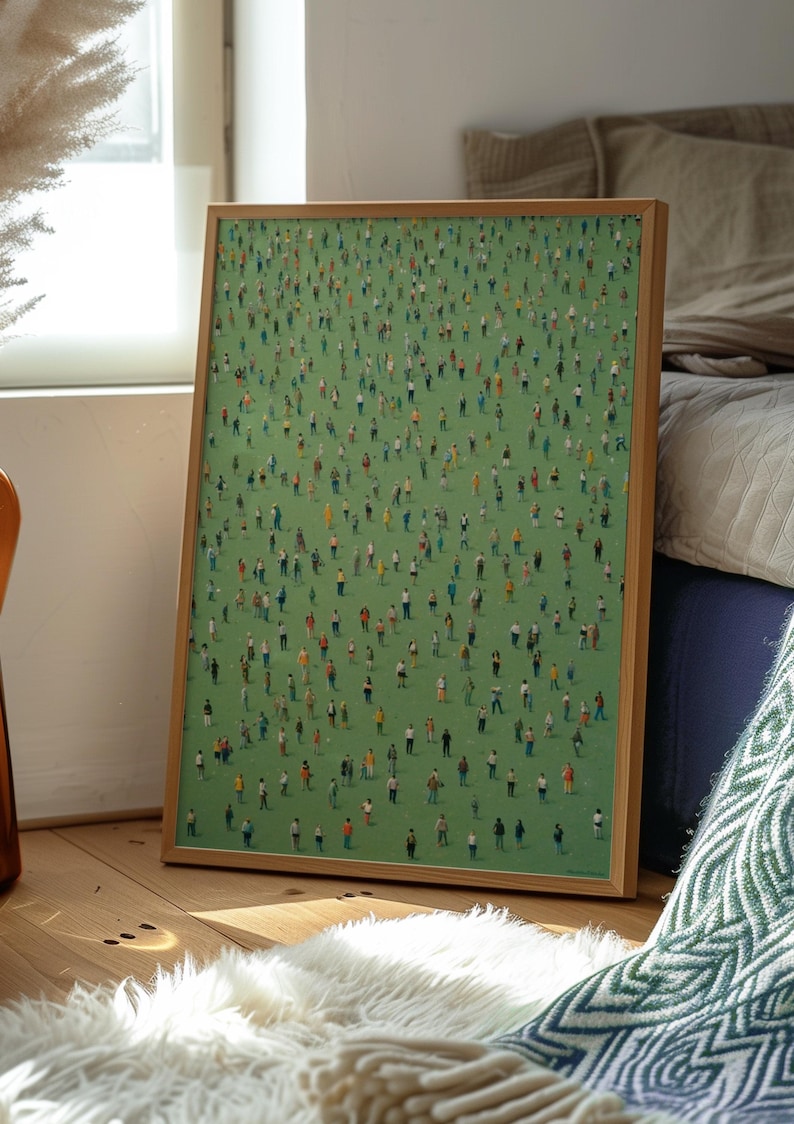 May include: A framed painting of a green field with many small figures of people standing on it. The frame is made of wood and has a light brown color.