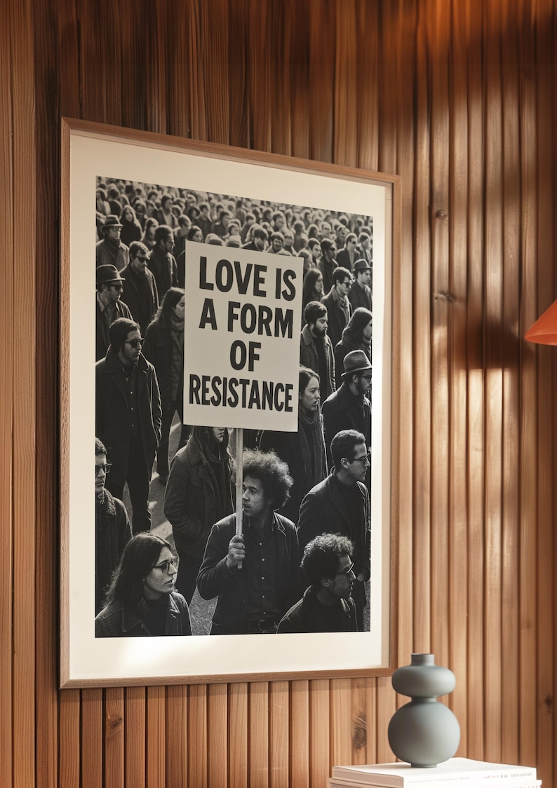 Pu&ograve; includere: Stampa incorniciata in bianco e nero con una folla di persone, con un cartello con la scritta "LOVE IS A FORM OF RESISTANCE". La stampa &egrave; esposta su una parete di legno, con un vaso decorativo.